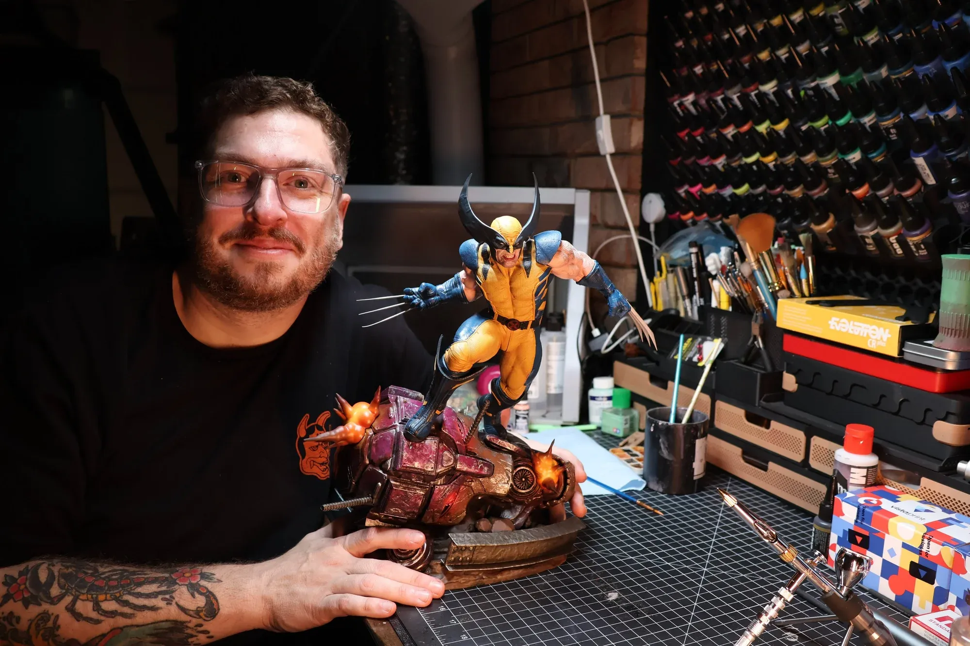 Ryan McHenry at the workbench, holding a hand-painted Wolverine statue amid his paints and brushes.
