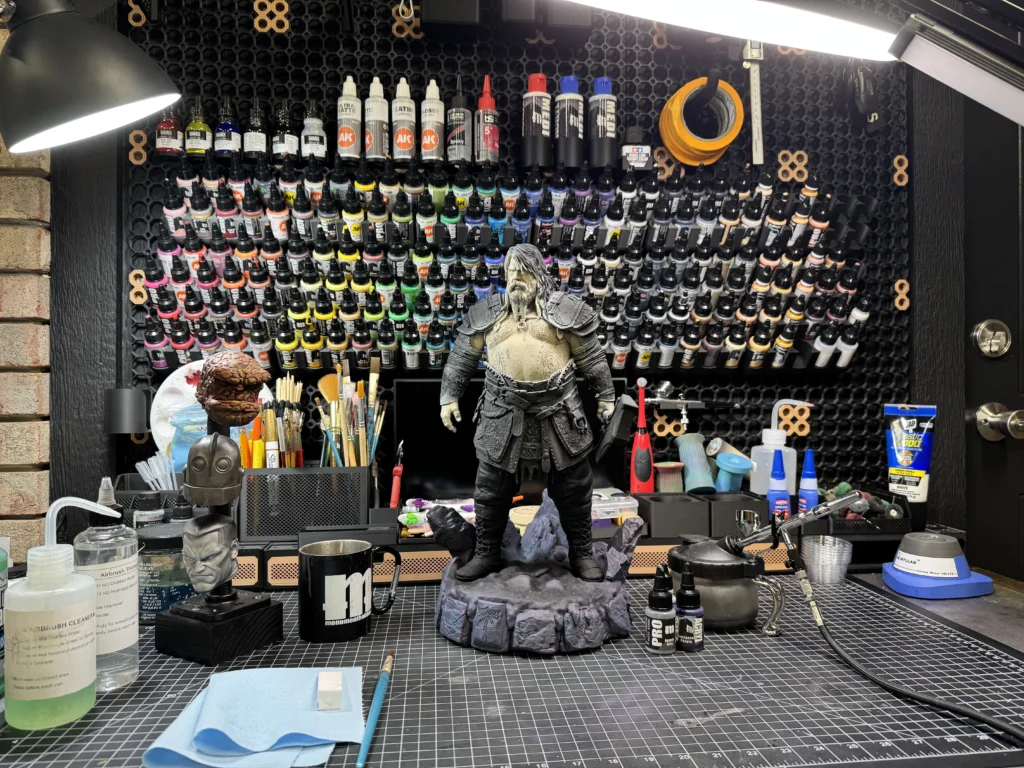 A packed miniature painting workstation with hundreds of paint bottles, brushes, and two turtle figures standing guard.